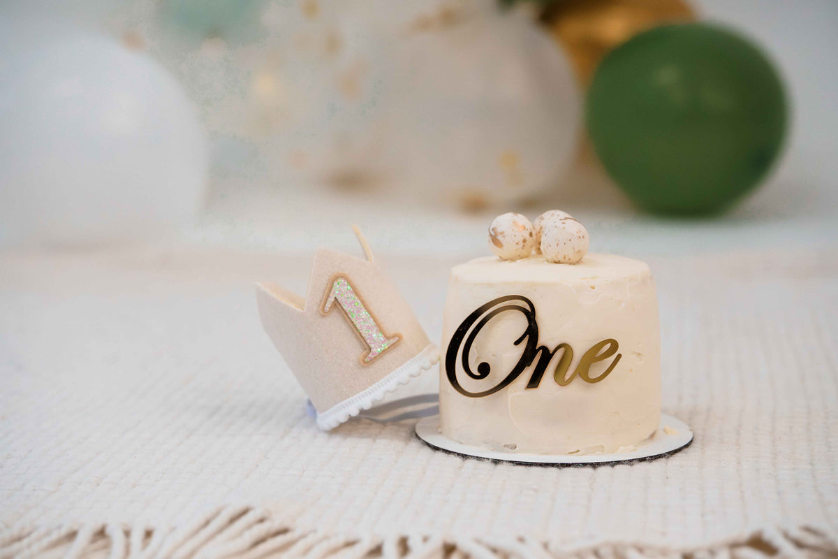 Small birthday cake with white icing, a number 1 cake topper.
